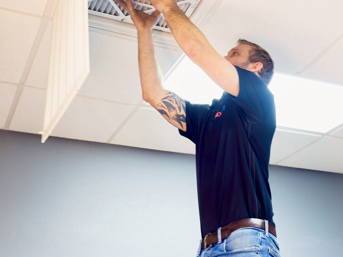 Excel technician reaching up to change a ceiling return filter, grille panel open beside him