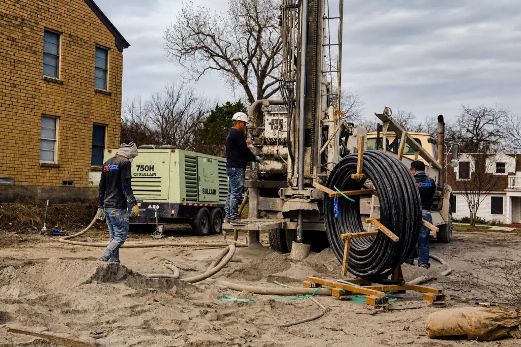 Excel Geothermal crew drilling a vertical well at a North Texas jobsite, with a reel of loop pipe staged beside the rig