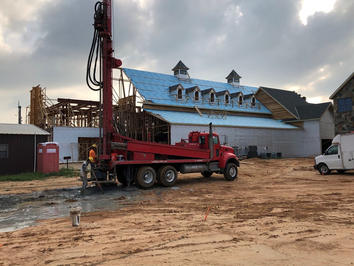 Excel Geothermal Versa-Drill rig boring wells beside a new-construction home, crew working at the bore