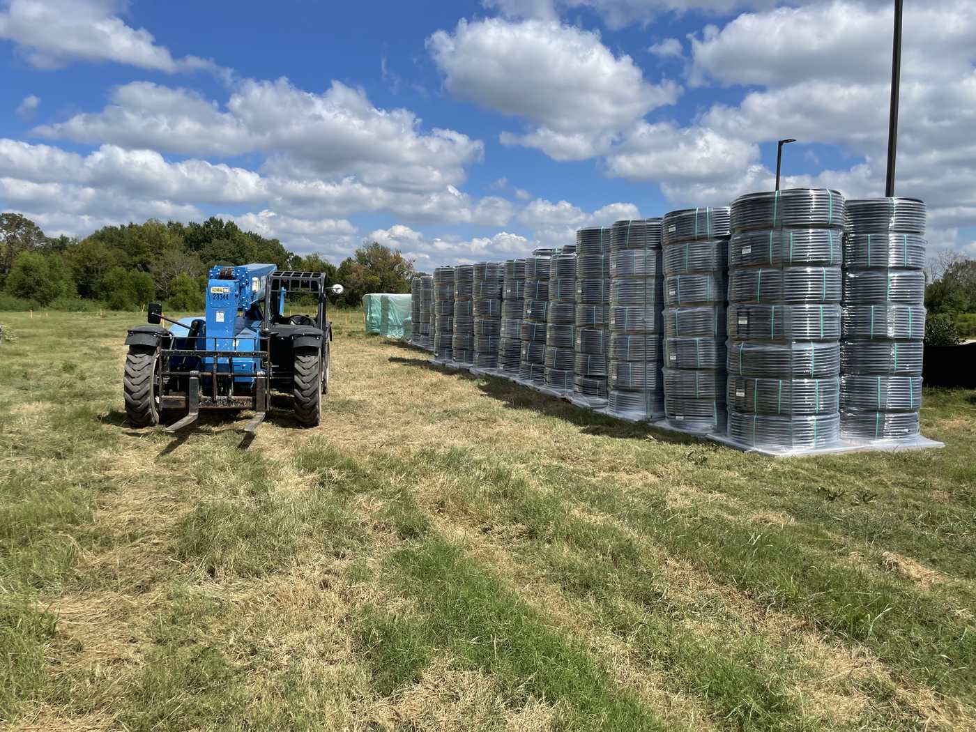 Pallets of coiled geothermal loop pipe staged in the field beside a telehandler before construction at Home2 Suites