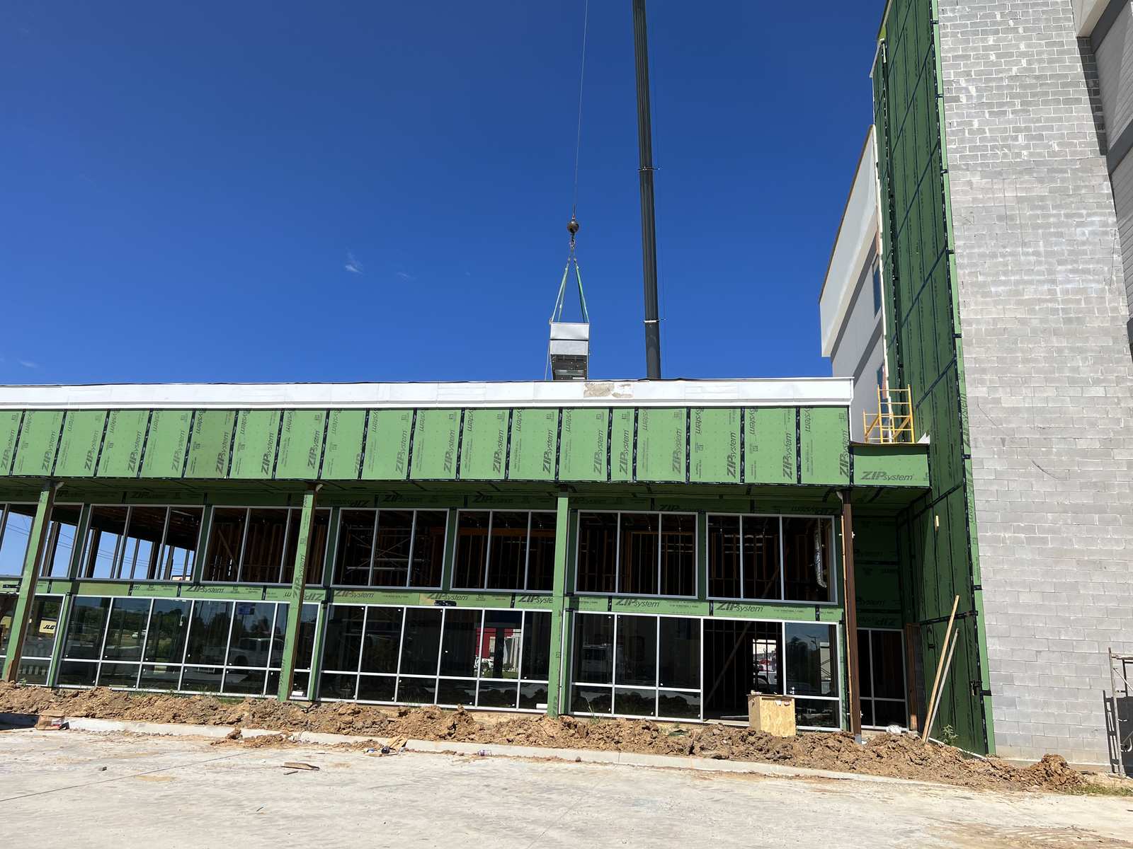 Crane lowering a heat-pump unit onto the low roof deck while the Home2 Suites building was still in sheathing