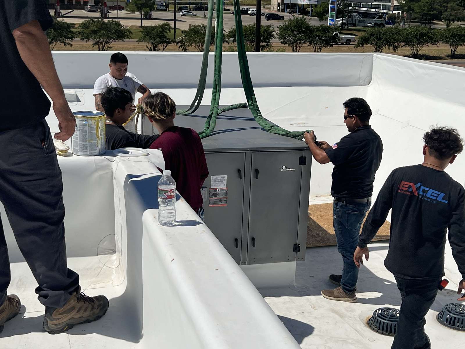 Excel crew guiding a ClimateMaster heat-pump unit lowered by crane onto the roof at Home2 Suites in Paris, Texas