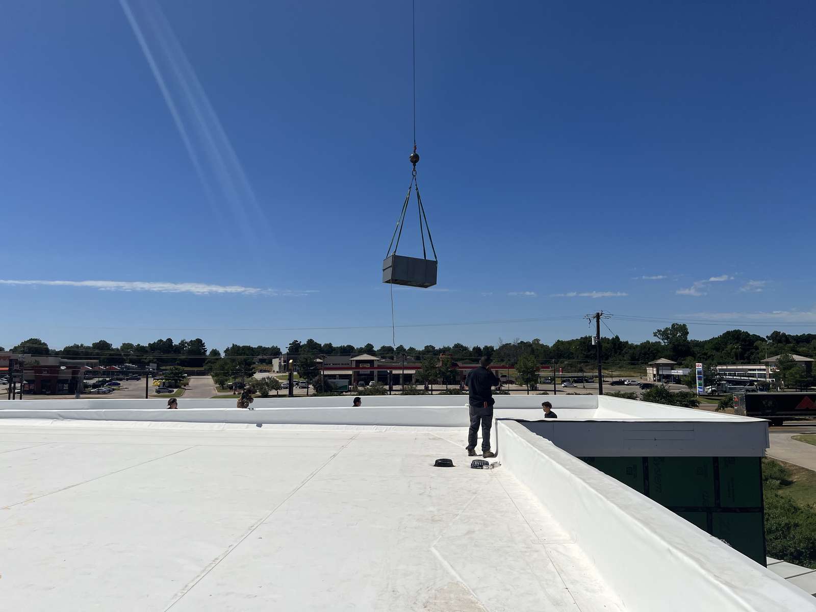 Heat-pump unit suspended from the crane hook high above the white membrane roof at Home2 Suites